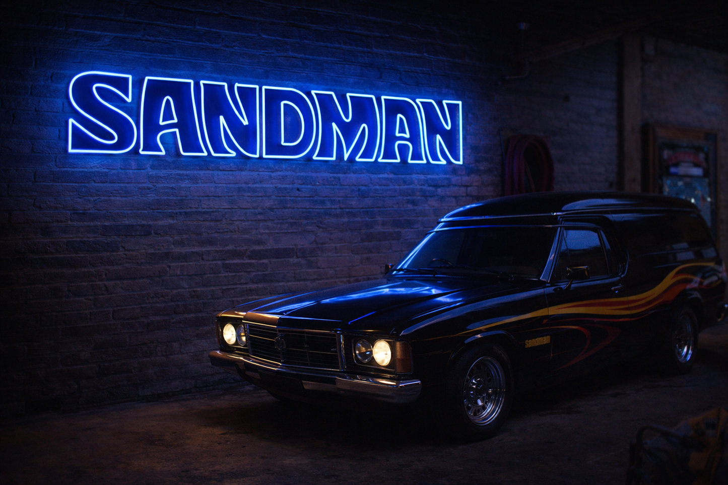 Vintage car in a dark setting with a neon sign reading 'Sandman' on a brick wall.