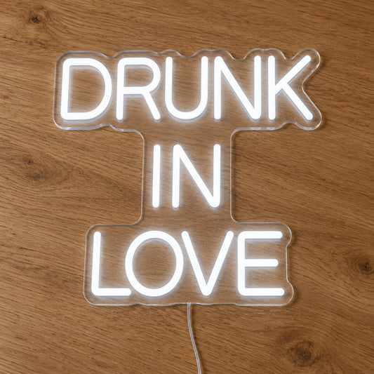 Drunk in Love LED Neon Light Sign in white, featuring three lines of block lettering on a wooden surface.
