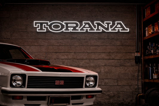 Vintage car with Torana logo neon sign and a picture of a Holden Torana against a textured wall.