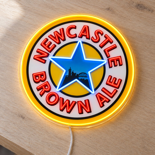 Newcastle Brown Ale LED Neon Sign, featuring beer-brand logo displayed on a wooden surface.