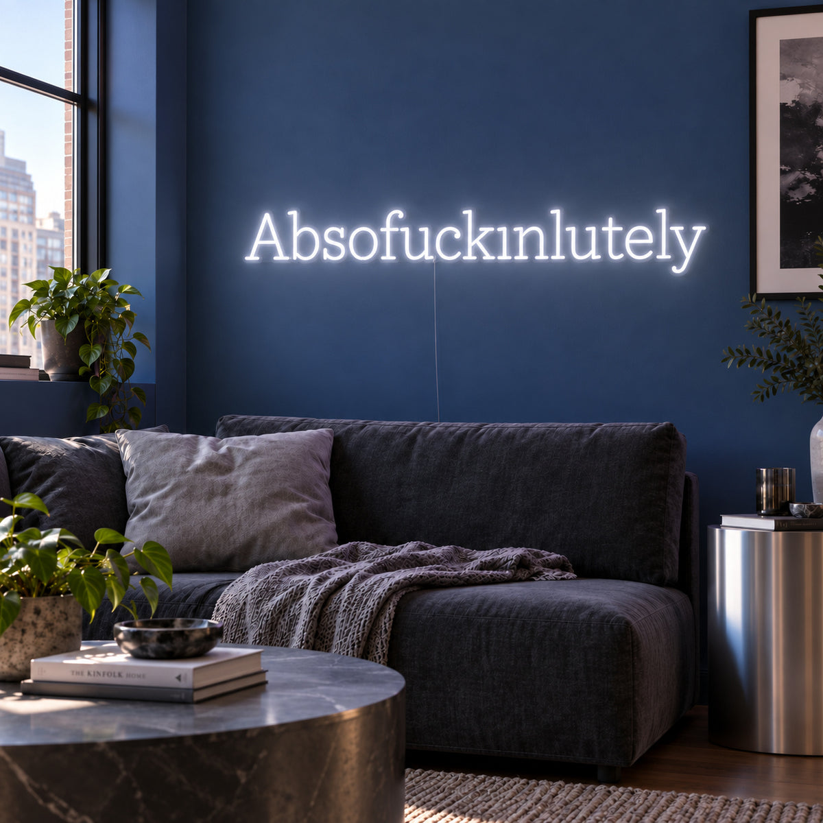 Absofuckinlutely Neon Sign glowing white above a charcoal sofa on a blue wall.