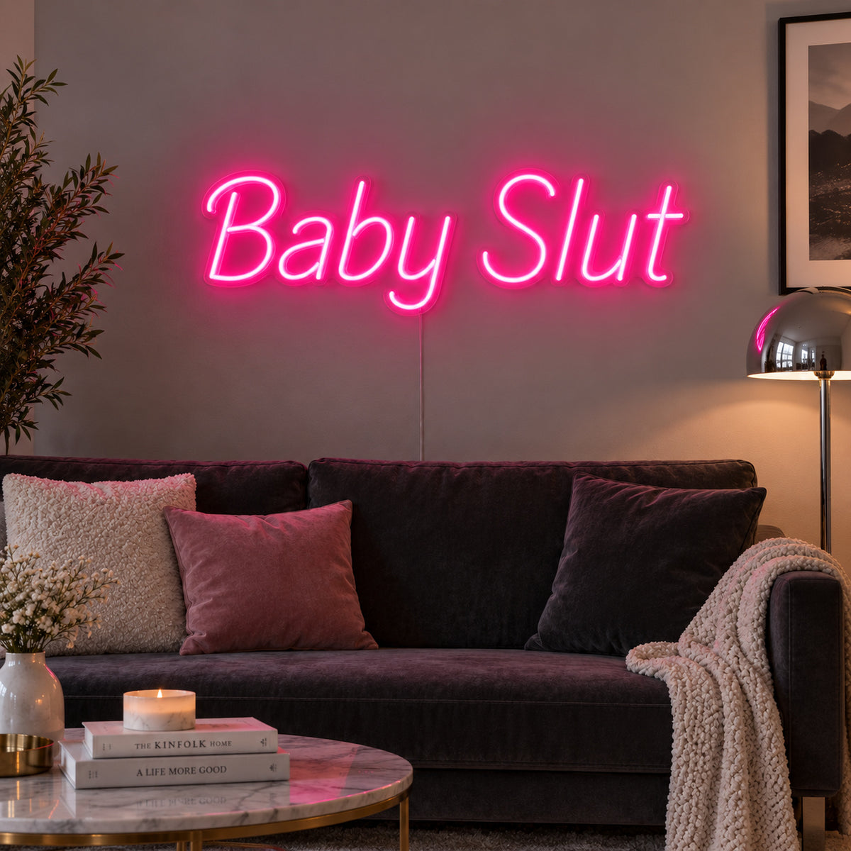 Rose Red version of the Baby Slut Neon Sign, shown above a grey sofa with pink cushions.