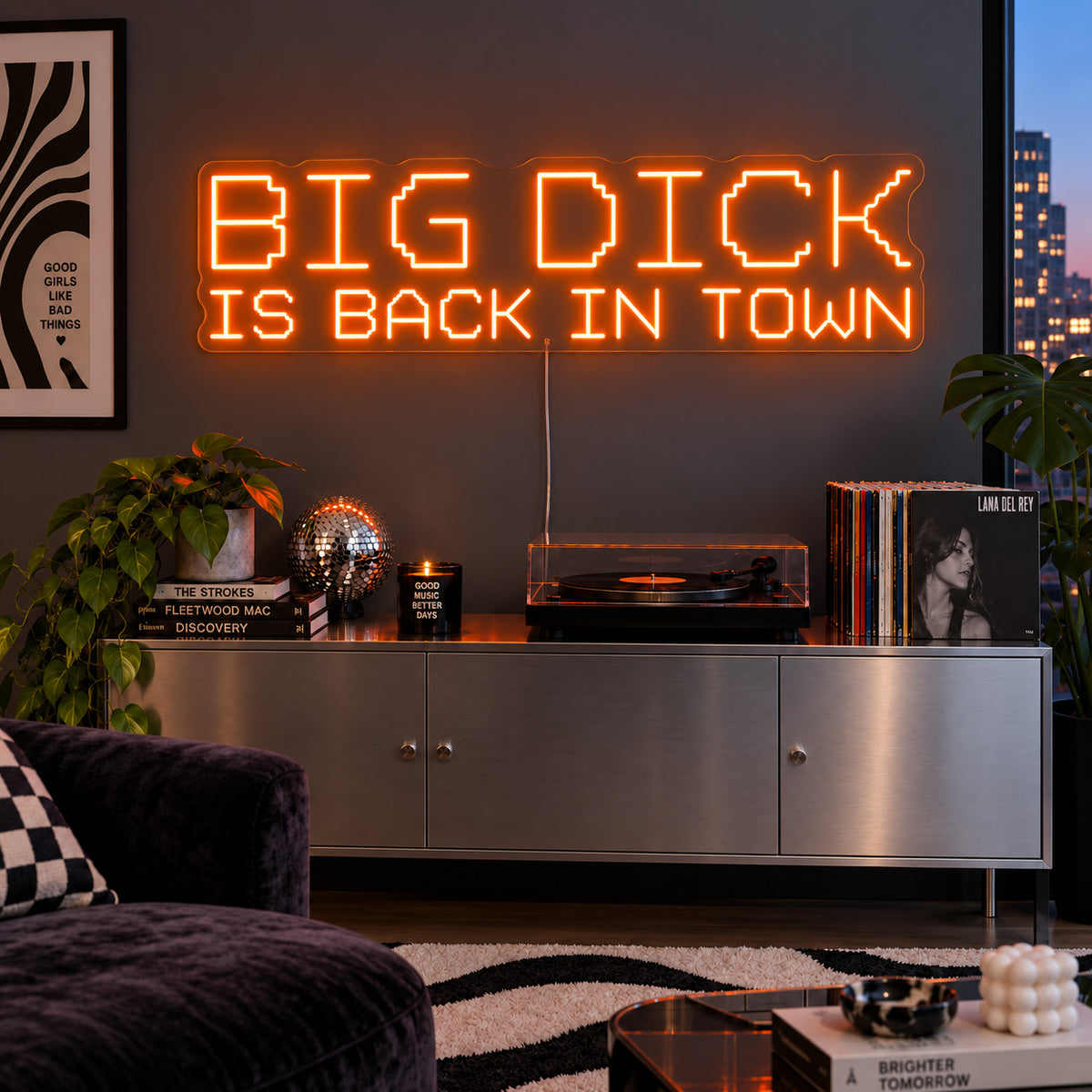 Orange version of the Big Dick Is Back In Town Neon Sign, shown above a record player and metal sideboard.