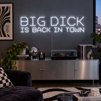 Big Dick Is Back In Town Neon Sign glowing white above a record player and metal sideboard.