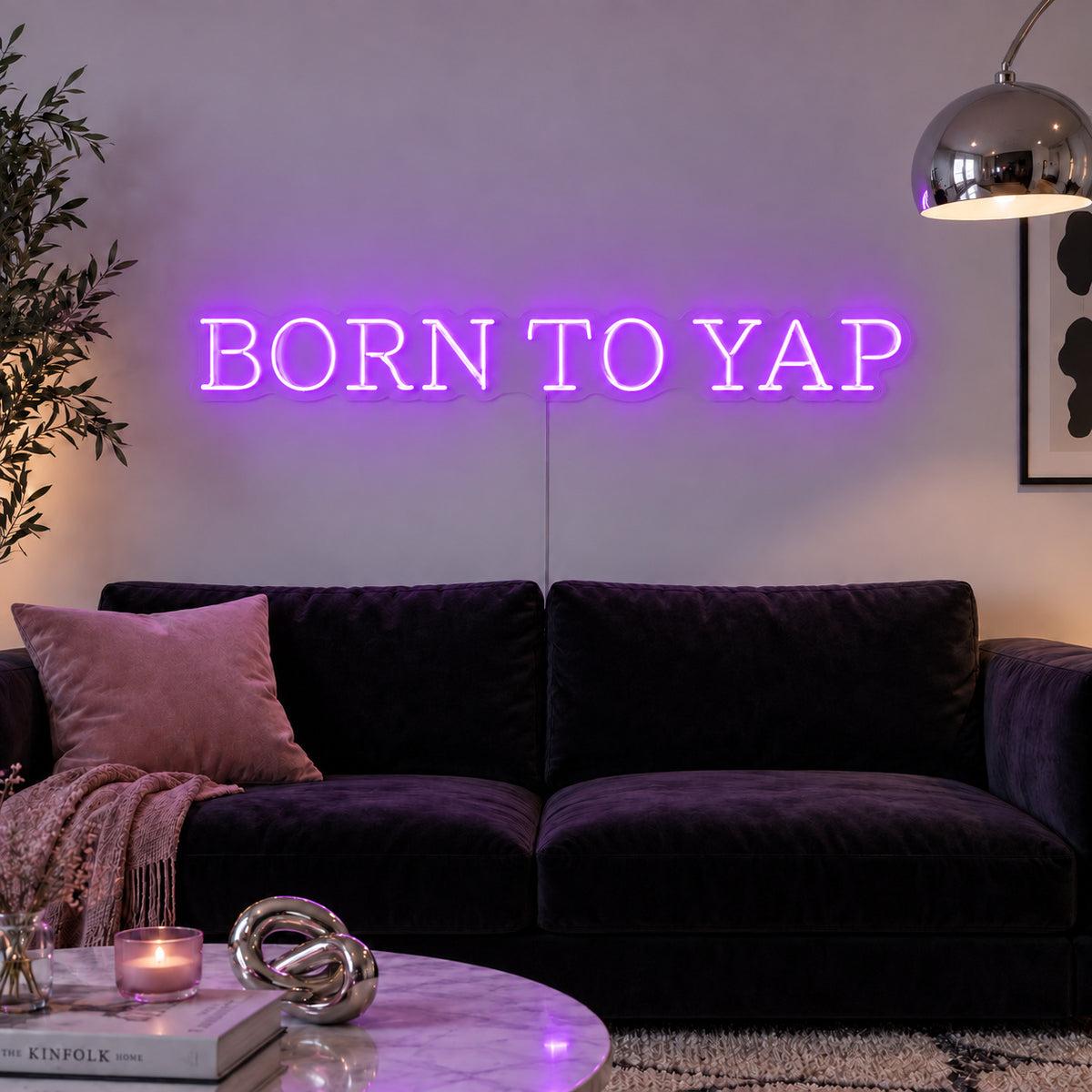Born To Yap Neon Sign with purple lighting, displayed above a dark sofa and glass coffee table.