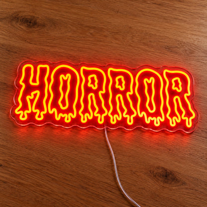 Horror Dripping Letters Neon Sign featuring the word Horror in orange outlined letters with dripping edges, illuminated on clear acrylic lying on a natural oak wooden surface.