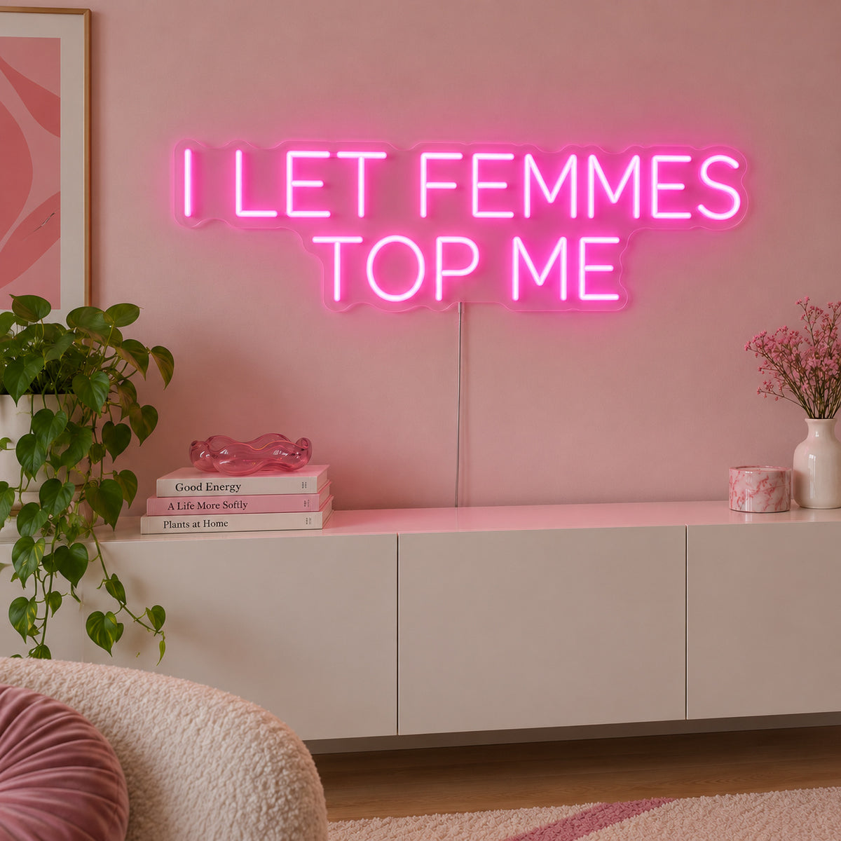 I Let Femmes Top Me Neon Sign glowing pink in rounded lettering above a white sideboard.