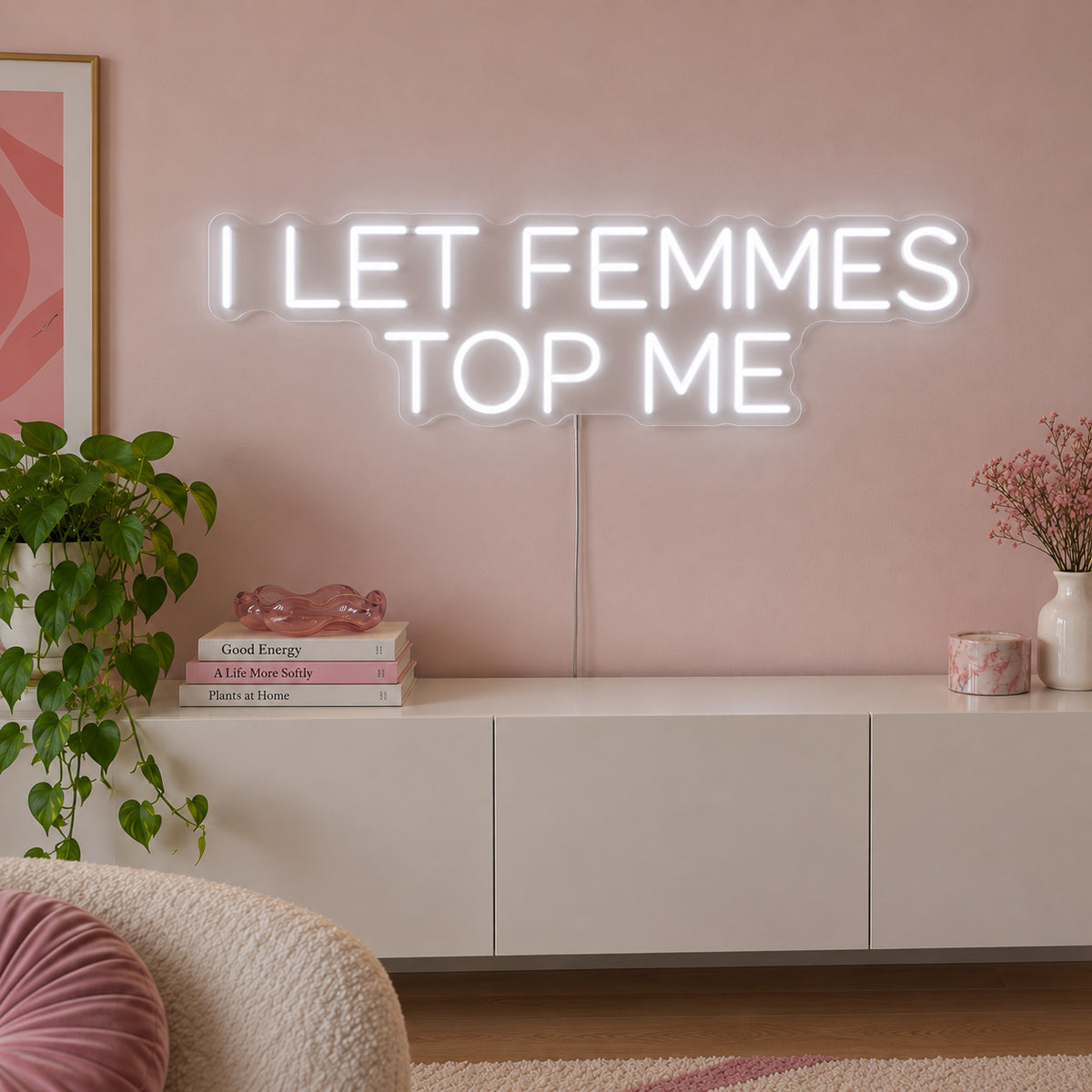 I Let Femmes Top Me Neon Sign glowing white in rounded lettering above a white sideboard.