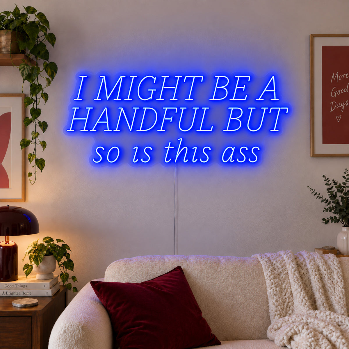 I Might Be A Handful But So Is This Ass Neon Sign glowing blue in wide lettering above a cream sofa.
