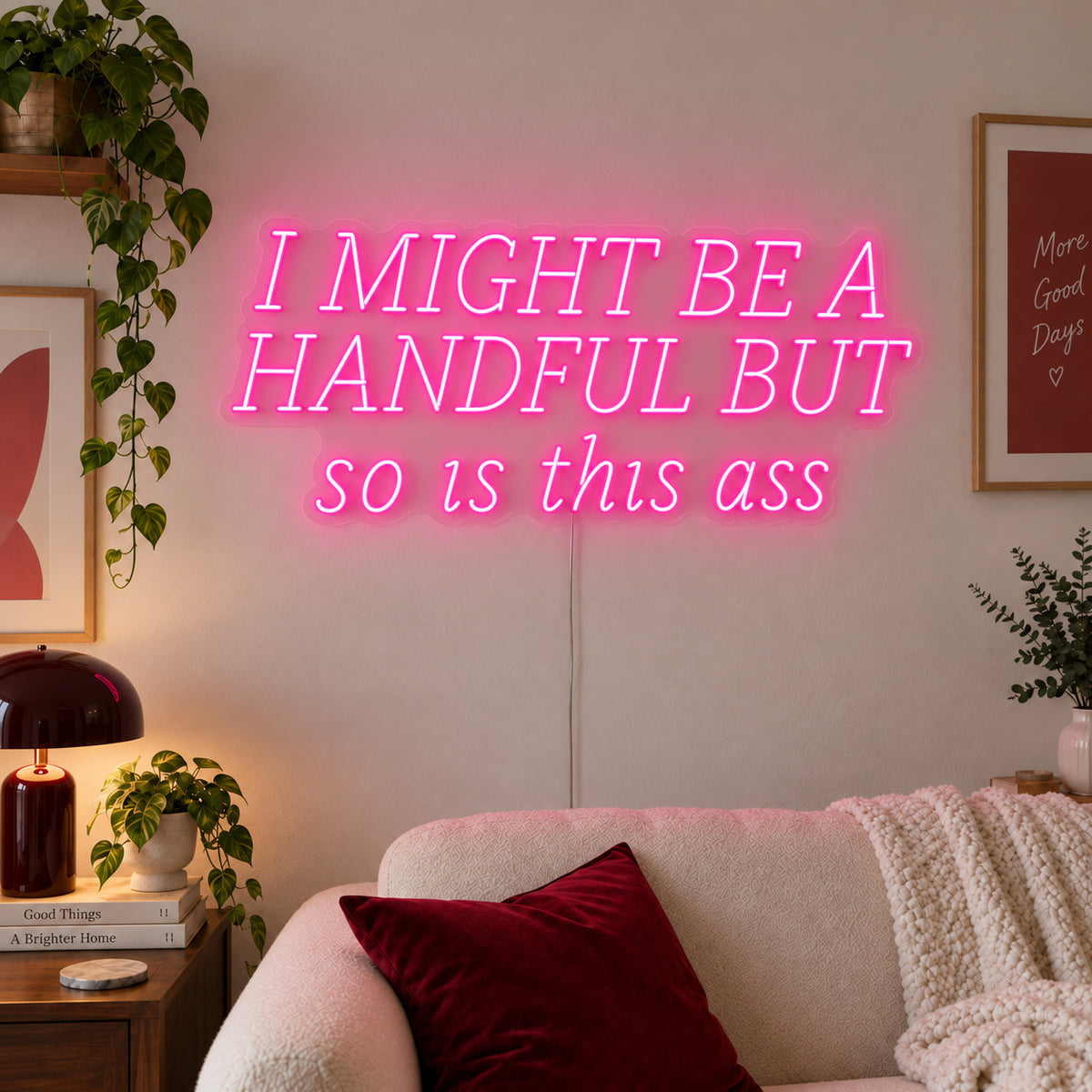 I Might Be A Handful But So Is This Ass Neon Sign glowing pink in wide lettering above a cream sofa.