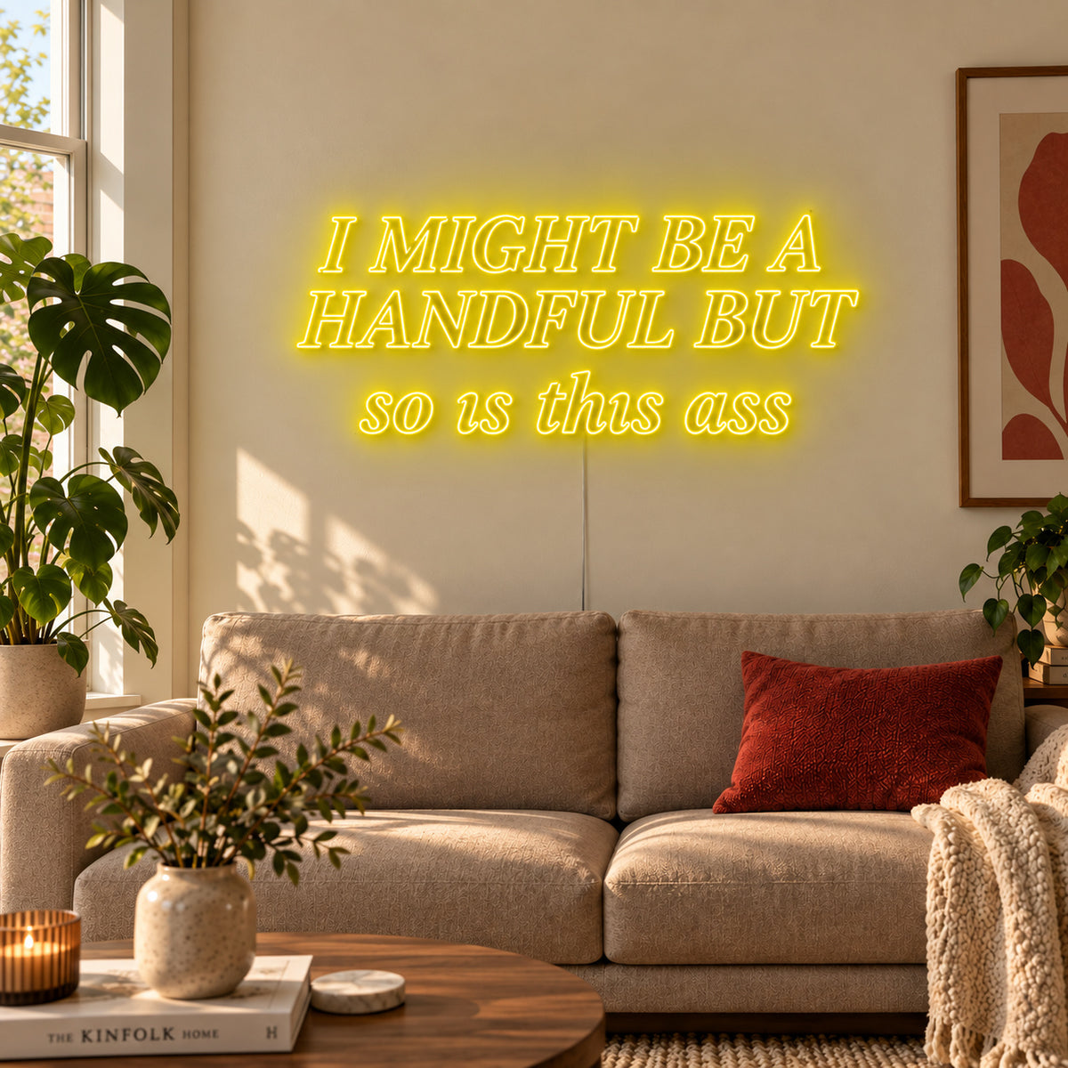 I Might Be A Handful But So Is This Ass Neon Sign with yellow lighting, displayed in compact lettering above a cream sofa.