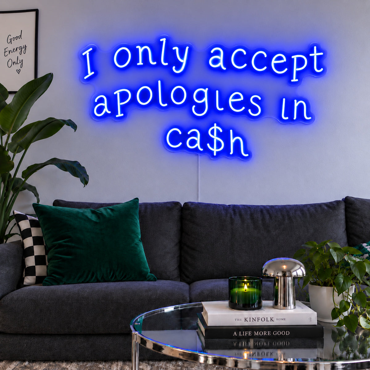 I Only Accept Apologies In Ca$h Neon Sign glowing blue above a charcoal sofa with green cushions.