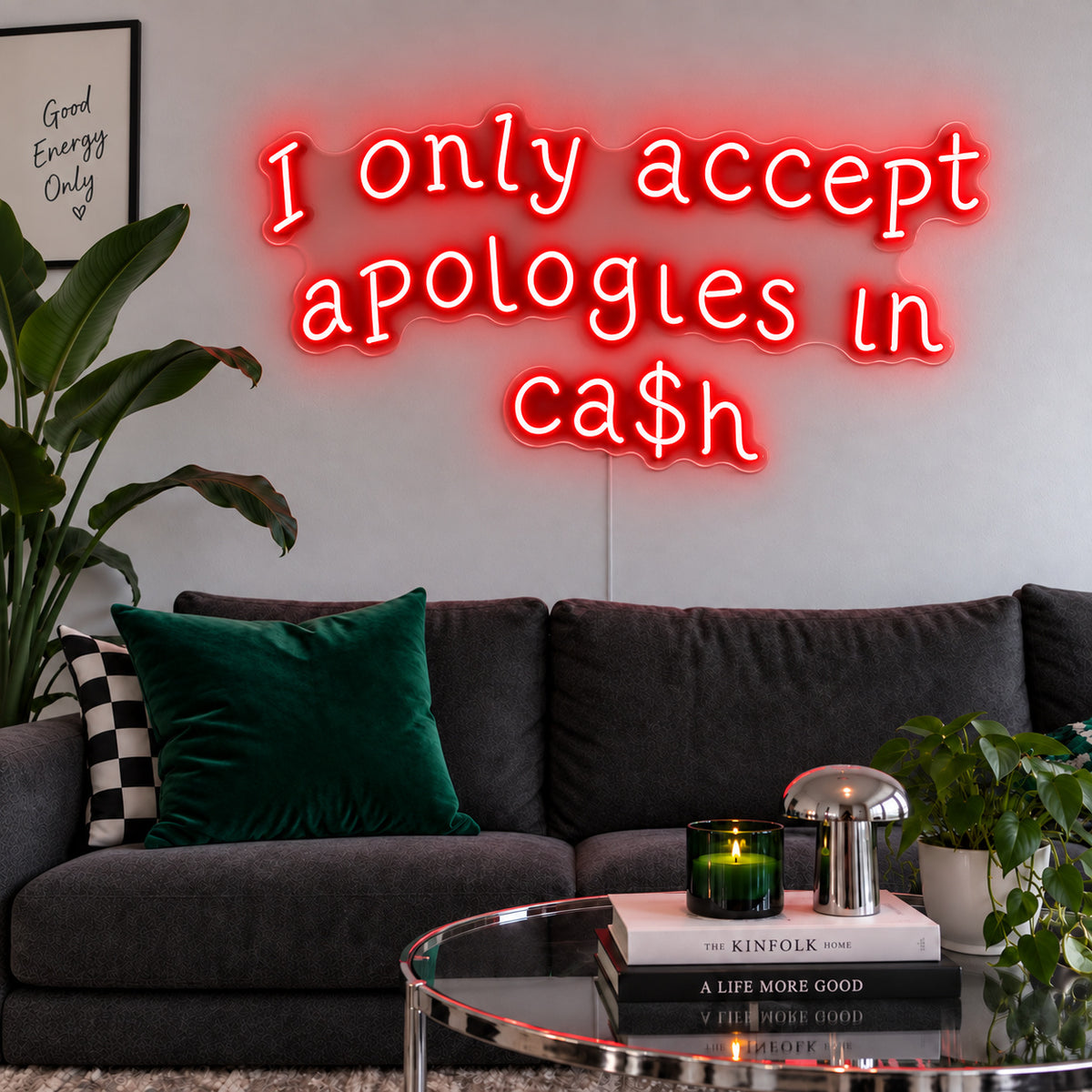 I Only Accept Apologies In Ca$h Neon Sign with red lighting, displayed above a charcoal sofa with green cushions.