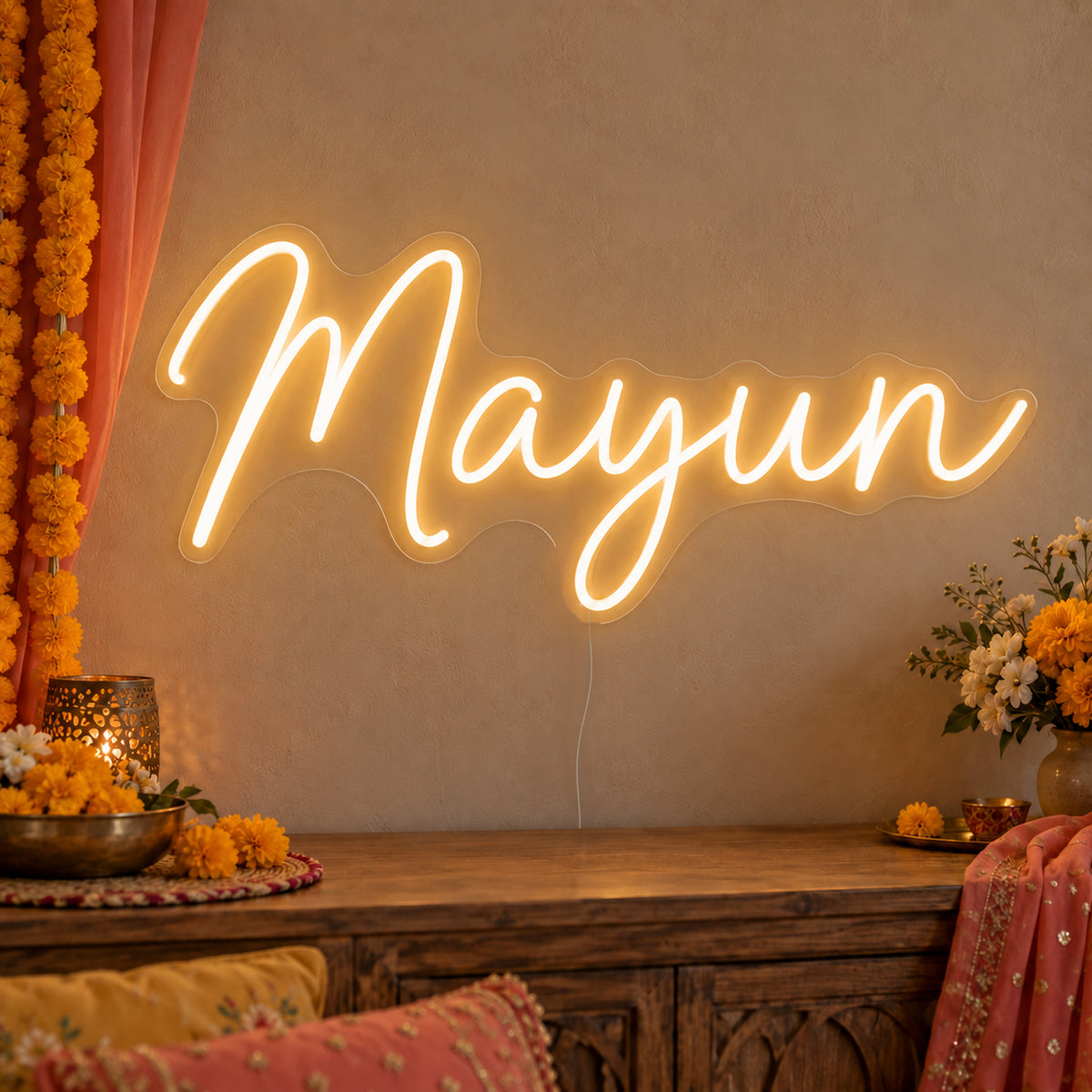 Mayun Neon Sign on clear cut-to-shape acrylic, illuminated on a wall in a styled celebration setting