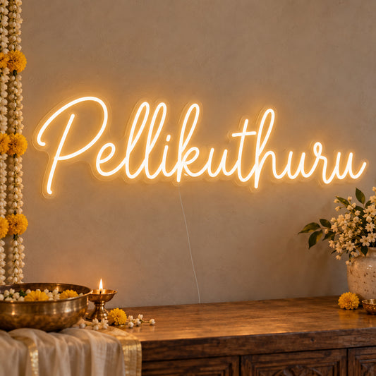 Pellikuthuru Neon Sign on clear cut-to-shape acrylic, illuminated on a wall in a styled celebration setting