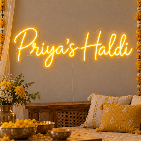 Personalised Haldi Neon Sign on clear cut-to-shape acrylic, illuminated on a wall in a styled celebration setting; sample personalised wording shown