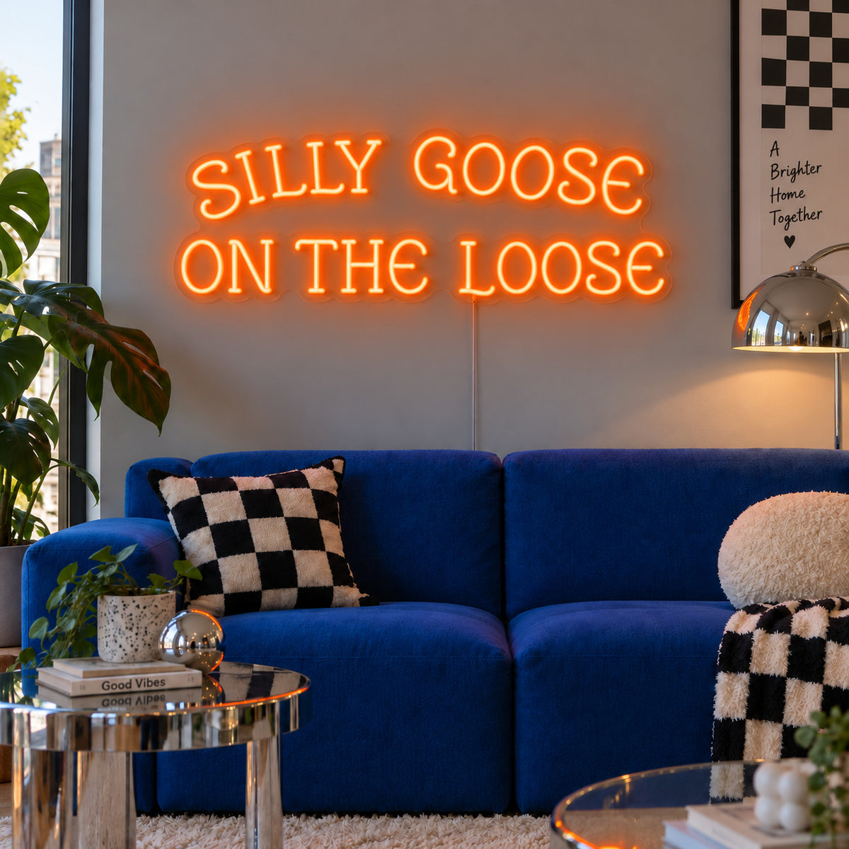 Orange version of the Silly Goose On The Loose Neon Sign, shown above a blue sofa with checkered cushions.